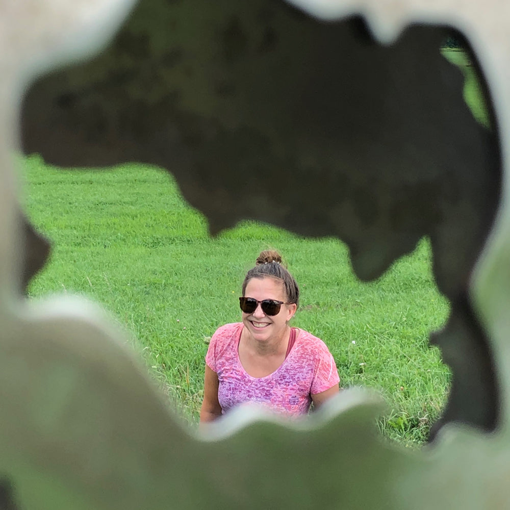 Heather Drury looking through a metal sculpture in a grassy field