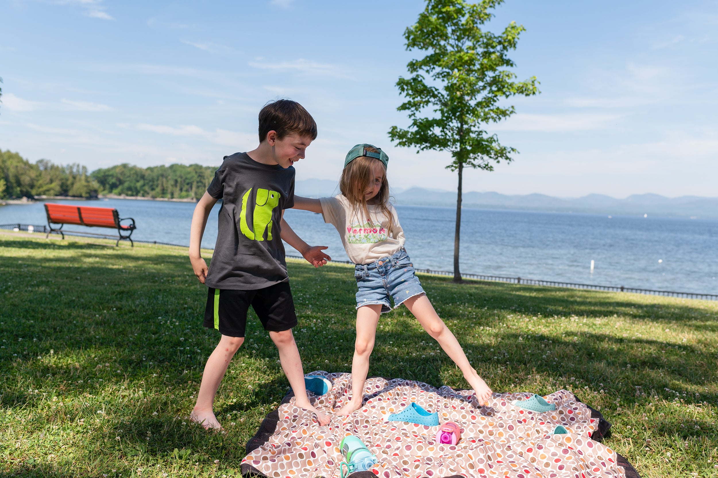 Two kids in Vermont Eclectic Company shirts playing in the grass along side Lake Champlain