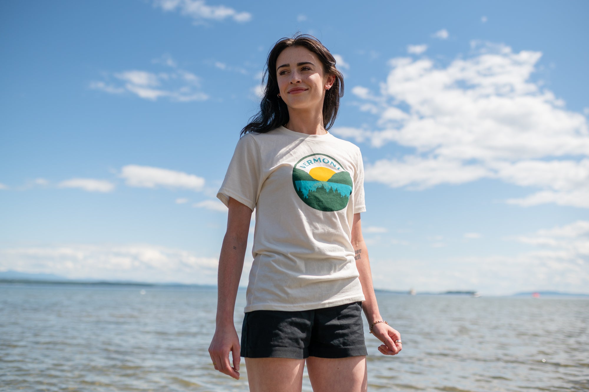 Woman standing in Lake Champlain with blue skies wearing a Vermont Eclectic Company shirt