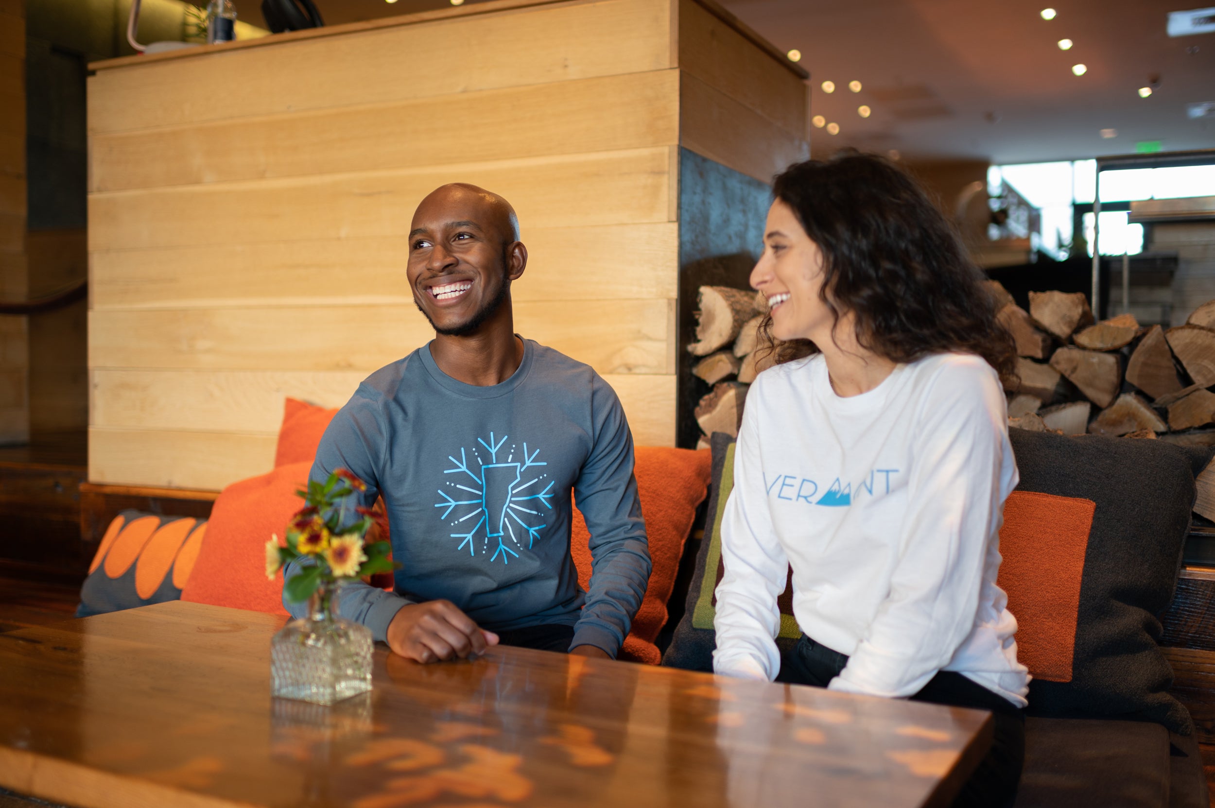 Man and woman sitting in a lounge wearing Vermont Eclectic Company shirts