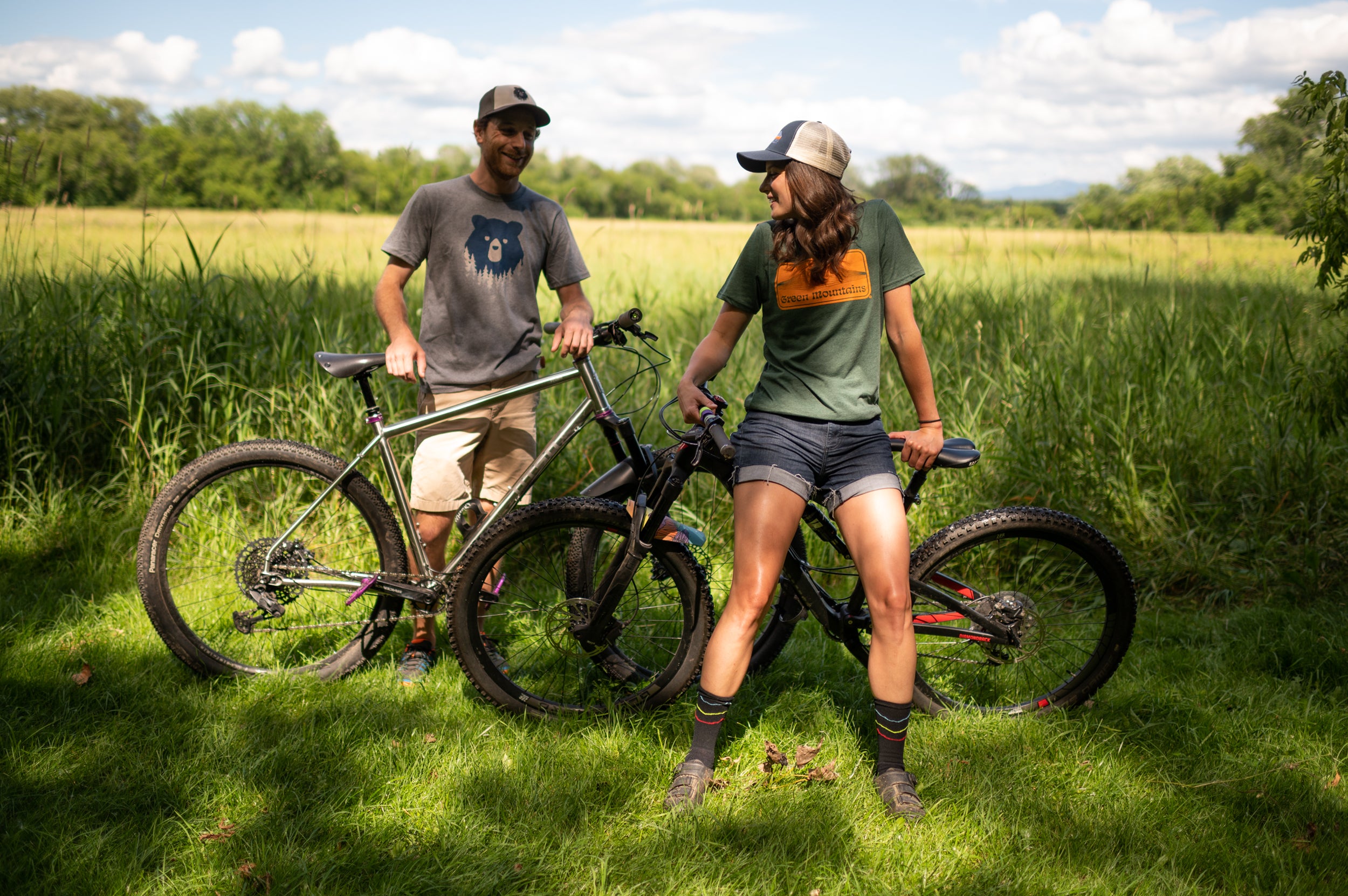 Two people leaning on bikes in a Vermont field while wearing Vermont Eclectic Company t-shirts